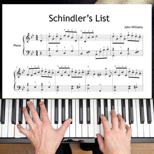May include: A sheet music page titled Schindler's List by John Williams, featuring black musical notation on a white background with finger numbering, positioned above a piano keyboard with black and white keys.