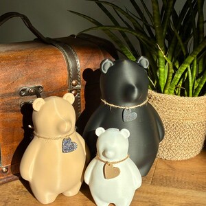 Pu&ograve; includere: Tre statuette a forma di orso in nero, beige e bianco. Ogni orso ha una finitura liscia e indossa una collana di spago con un piccolo ciondolo a forma di cuore. L'orso nero &egrave; il pi&ugrave; grande, seguito dall'orso beige e l'orso bianco &egrave; il pi&ugrave; piccolo.