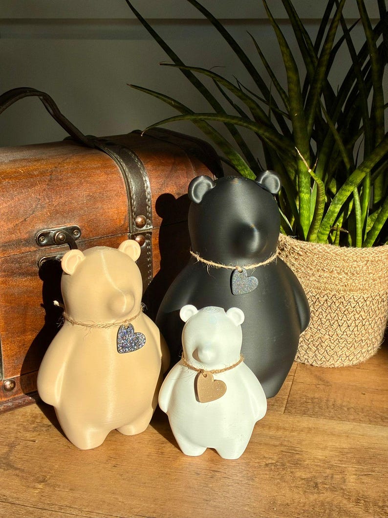 Pu&ograve; includere: Tre statuette a forma di orso in nero, beige e bianco. Ogni orso ha una finitura liscia e indossa una collana di spago con un piccolo ciondolo a forma di cuore. L'orso nero &egrave; il pi&ugrave; grande, seguito dall'orso beige e l'orso bianco &egrave; il pi&ugrave; piccolo.
