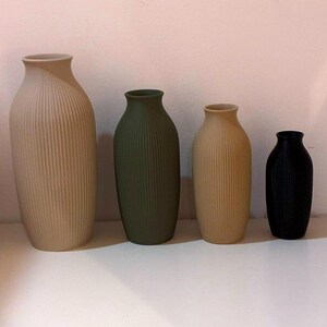 May include: Four ceramic vases in varying sizes and colors. The largest is beige, the next is olive green, followed by a smaller beige vase, and the smallest is black. All vases have vertical ribbed detailing.