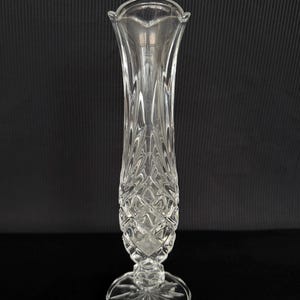 Può includere: Vaso di vetro trasparente con parte superiore svasata e motivo a taglio diamante. Il vaso ha una base rotonda con un motivo a stella. Il vaso è alto circa 25 cm.