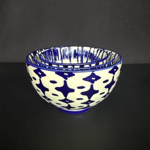 May include: Set of three ceramic bowls with a cream-colored base and a blue starburst pattern. The bowls have a blue rim and base, and are nested together. The bowls are on a black surface.