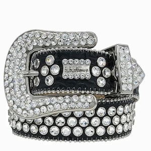 Puede incluir: Un cinturón de cuero negro con hebilla y detalles plateados. La hebilla y el cinturón están incrustados con pedrería transparente. El cinturón tiene el texto "B.B. Simon" en el cuero.