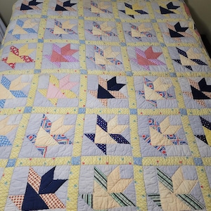 May include: A patchwork quilt featuring a repeating basket block pattern. Each block consists of light blue fabric squares with various patterned and solid-colored fabric pieces forming basket shapes, separated by yellow sashing.