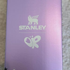 May include: A lavender box with a star pattern and the Stanley logo. The box features a stylized emblem and the letters "OR". The stars are in red, white, and black.