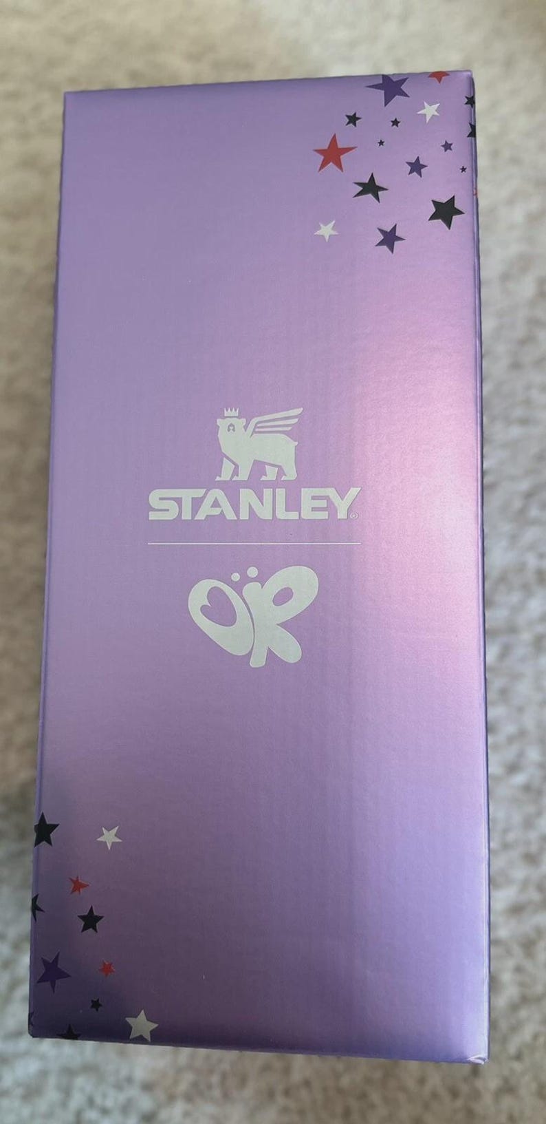 May include: A lavender box with a star pattern and the Stanley logo. The box features a stylized emblem and the letters "OR". The stars are in red, white, and black.