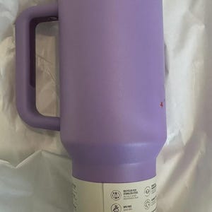 May include: A lavender insulated travel mug with a handle and a lid. The mug is made of stainless steel and has a capacity of approximately 30 ounces. The mug has a handle and a lid. The mug is BPA free, splashproof, and dishwasher safe.