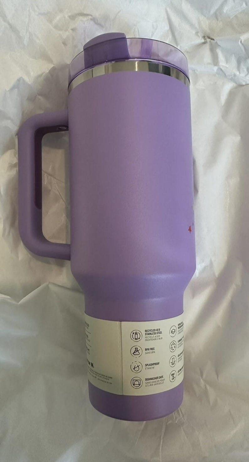 May include: A lavender insulated travel mug with a handle and a lid. The mug is made of stainless steel and has a capacity of approximately 30 ounces. The mug has a handle and a lid. The mug is BPA free, splashproof, and dishwasher safe.