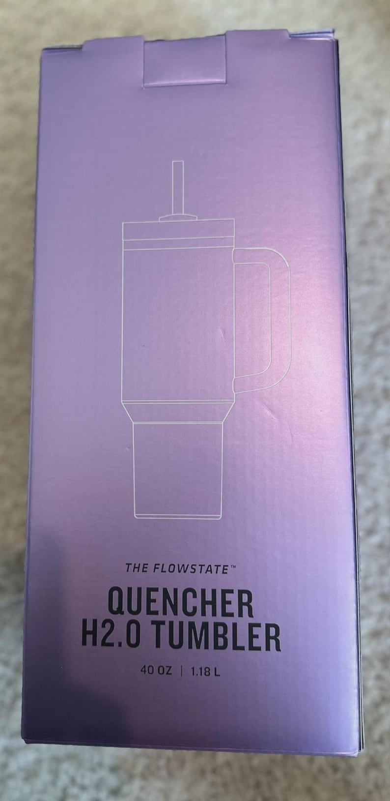 May include: A lavender box featuring a line drawing of a tumbler with a handle and straw. The text reads "THE FLOWSTATE QUENCHER H2.0 TUMBLER" and indicates a 40 oz capacity.