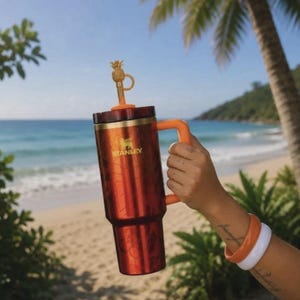 May include: A metallic orange Stanley tumbler with a handle and a gold-colored pineapple-shaped straw topper. The cylindrical cup features the Stanley logo in gold lettering on the front, a dark lid, and a matching orange straw extending from the top.