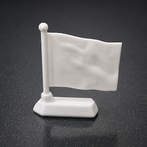 May include: A small, white ceramic flag on a white pole, set on a rectangular base. The flag has a slightly textured appearance, and the pole is topped with a small sphere. The background is a dark, speckled surface.