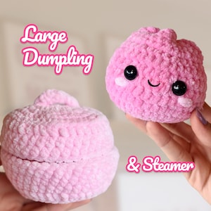 Könnte beinhalten: Ein rosa gehäkeltes Plüsch-Knödel mit schwarzen Sicherheitsaugen und einem lächelnden Gesicht, gepaart mit einem passenden rosa gehäkelten Dampfgarer-Korb mit Deckel. Der Text Large Dumpling & Steamer ist in rosa und weißer Schrift zu sehen.