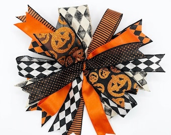 Op de afbeelding: Een decoratieve Halloween-strik met verschillende linten in oranje, zwart en wit. De strik bevat linten met pompoenen, stippen, strepen en ruitpatronen. Perfect voor feestelijke vakantiedecoraties.