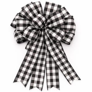 May include: A large decorative bow in a black and white buffalo check pattern. The bow features multiple loops and long, pointed tails, ideal for adding a touch of rustic charm to any decor. The bow is made of fabric.
