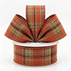 May include: A spool of wired ribbon featuring a plaid pattern in shades of burnt orange, sage green, and thin navy blue lines. The ribbon is arranged in a fan shape at the top, showcasing the woven texture and the consistent grid design throughout.