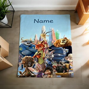 May include: A light blue blanket featuring a group of animated animal characters from a movie, with a cityscape backdrop. The word "Name" is written in dark blue at the top. The blanket is rectangular.