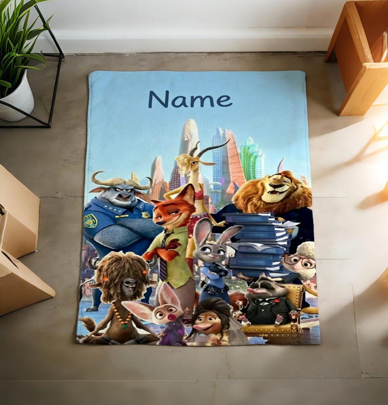 May include: A light blue blanket featuring a group of animated animal characters from a movie, with a cityscape backdrop. The word "Name" is written in dark blue at the top. The blanket is rectangular.
