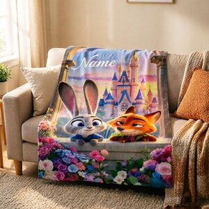 May include: A soft blanket featuring Judy Hopps and Nick Wilde from Zootopia, with a castle backdrop and the word "Name" in script. The blanket is decorated with colourful flowers and is draped over a sofa.