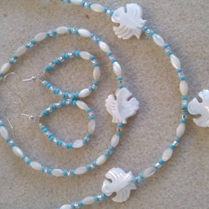 May include: A set of white shell and turquoise bead jewelry featuring a necklace, earrings, and a pendant. The pendant is shaped like a fish and has a carved design.