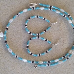 May include: A turquoise and black beaded necklace with a white shell pendant and matching earrings. The necklace has a silver clasp.