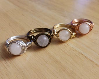 May include: Four wire-wrapped rings with clear quartz stones. The rings are made with silver, gold, and rose gold wire.