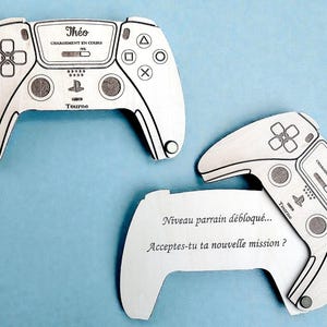 Peut inclure: Trois découpes en bois représentant des manettes de jeu, avec des détails gravés en noir. Deux manettes sont entières, et l'une a une bulle de dialogue avec du texte en français. Les manettes portent le nom "Théo" et le texte "CHARGEMENT EN COURS".