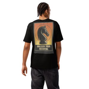 May include: Black t-shirt featuring a chess knight graphic within a rectangular frame. The design includes a black knight on a yellow and orange gradient background, with the text "UNLEASH YOUR POTENTIAL" below the knight. The shirt is made of a soft material.
