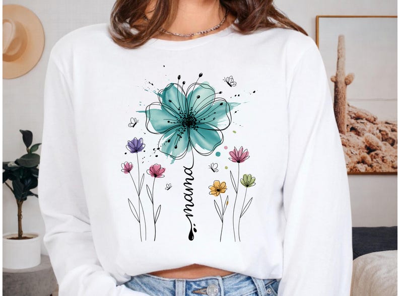 May include: White long-sleeve sweatshirt featuring a watercolor floral design. A large teal flower is at the top, with the word "mama" written vertically below it. Smaller colorful flowers and butterflies are also present.