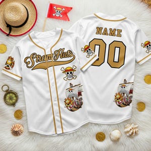 May include: White baseball jersey with gold accents, featuring "Straw Hats" text and pirate-themed graphics. The jersey has a button-up front, short sleeves, and the number "00" on the back. A straw hat and flag with a skull and crossbones are also visible.