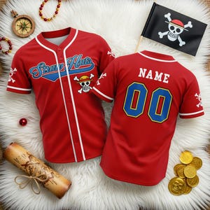 以下が含まれることがあります： 青い文字で「Straw Hats」とスカルとクロスボーンのロゴが入った赤い野球ジャージ。背面には、金色の縁取りと海賊旗が付いた青色の数字「00」が表示されています。