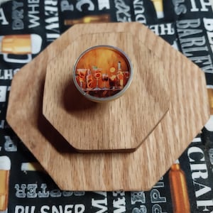 May include: A wooden coaster set with three octagonal pieces. The top coaster has a silver-rimmed image of cocktails. The coasters are made of light brown wood, and the background has a black and white pattern with beer-related text.