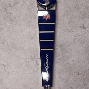 May include: A blue and silver Bud Light beer tap handle with the NFL logo. The handle has a circular top with the Bud Light logo and a football design. The main body is blue with white stripes and the Bud Light logo.