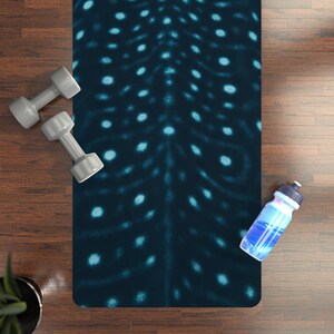 May include: A dark blue yoga mat with a pattern of light blue dots and lines. Two gray dumbbells and a water bottle are on the wooden floor next to the mat. A small green plant is in the lower left corner.