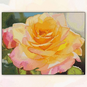 May include: A cross-stitch pattern depicting a large, open yellow and pink rose. The central petals are a rich orange, fading to soft pink at the edges. Green leaves and a touch of blue suggest a sunny day. The design is framed in black.