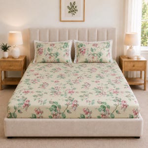 Puede incluir: Una cama con una sábana bajera de color crema y dos fundas de almohada a juego, decoradas con un patrón repetitivo de flores rosas y hojas verdes. Las fundas de almohada tienen un delicado borde de encaje blanco en los extremos.