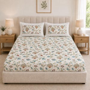 May include: A bed featuring a cream-coloured fitted sheet and two matching rectangular pillows, all decorated with a repeating floral pattern in shades of blue, green, and muted red. The pillows are finished with a white scalloped lace trim.