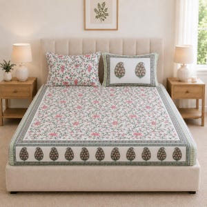 May include: A bed set featuring a white fitted sheet and two pillowcases with a floral vine pattern in pink and green. The sheet has a border with a repeating paisley motif in dark green and pink. One pillowcase matches the sheet, while the other features a white centre with two paisley designs.