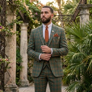 May include: A three-piece green and brown plaid suit with a white dress shirt and orange tie. The suit includes a matching vest, pocket square, and lapel pin. The suit is tailored and worn outdoors.