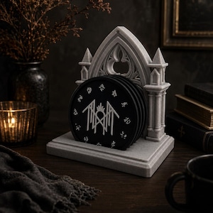 Peut inclure: Ensemble de dessous de verre noirs avec un motif graphique blanc, empilés dans un support gris de style gothique. Les dessous de verre sont de forme circulaire et sont présentés sur une surface en bois, avec une bougie et des objets décoratifs en arrière-plan.