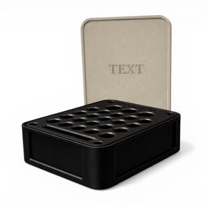 Puede incluir: Un organizador rectangular negro con múltiples agujeros circulares, posiblemente para guardar objetos. Una tapa beige con la palabra "TEXTO" está detrás del organizador. El diseño es moderno y minimalista.