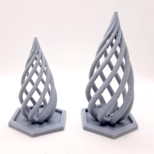 May include: Two gray, abstract sculptures with a woven, teardrop design. Each sculpture sits on a hexagonal base. The larger sculpture is approximately 6 inches tall, while the smaller one is about 4 inches tall. The sculptures are made of a solid, matte material.