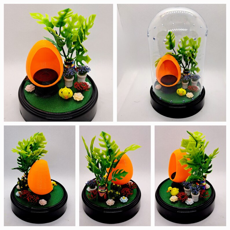 May include: A miniature orange chair with a green plant and a small yellow bird figurine inside a clear glass dome. The base of the dome is black and the scene is set on a green base.