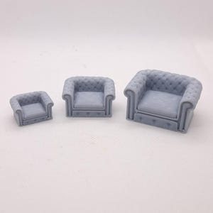 May include: Three miniature gray armchairs of varying sizes are arranged in a row. Each chair features a button-tufted back and seat, with rolled arms and a rectangular base. The smallest chair is a square shape, while the largest has a more rectangular seat.