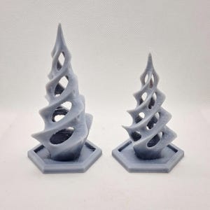 May include: Two gray, abstract sculptures with a spiral design and open spaces. Each sculpture sits on a hexagonal base. The forms have a textured appearance and are set against a white background.