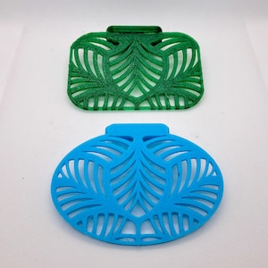 May include: Two decorative air freshener holders. One is square and green, the other is oval and blue. Both have a cut-out leaf design. The holders have a tab on top for hanging.
