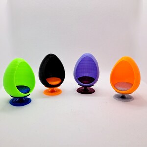 May include: Four miniature egg-shaped chairs in different colours: green, black, purple, and orange. Each chair has a round base and a small seat.