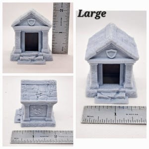 May include: A light gray miniature tomb with a shield emblem above the entrance. The model has a textured, stone-like appearance and is labeled "Large". A ruler is placed next to the model for scale.