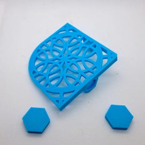 May include: A bright blue, corner-shaped decorative piece with a geometric, openwork design. Two small, blue, hexagonal pieces are also present. The corner piece has a small, cylindrical projection on the bottom. The objects are made of a solid material.