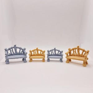 May include: Four miniature benches in varying colors: two gray, one yellow, and one brown. The benches have a rustic, twig-like design, perfect for a fairy garden or dollhouse setting. Each bench has a backrest and four legs.