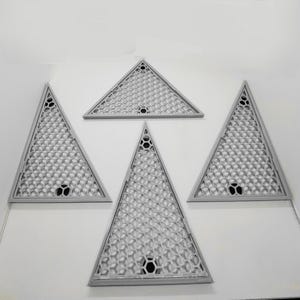 May include: Four gray, triangular decorative panels with a honeycomb pattern and a black circular hole in the center. The panels are arranged on a white surface.